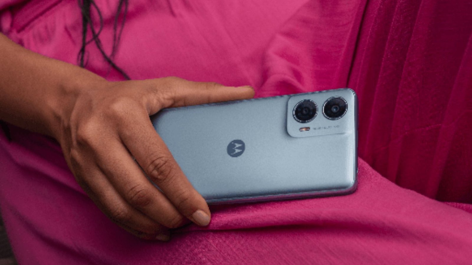 Mão feminina de pele preta usando roupa rosa segura um Motorola Moto G24 Power na cor azul celeste
