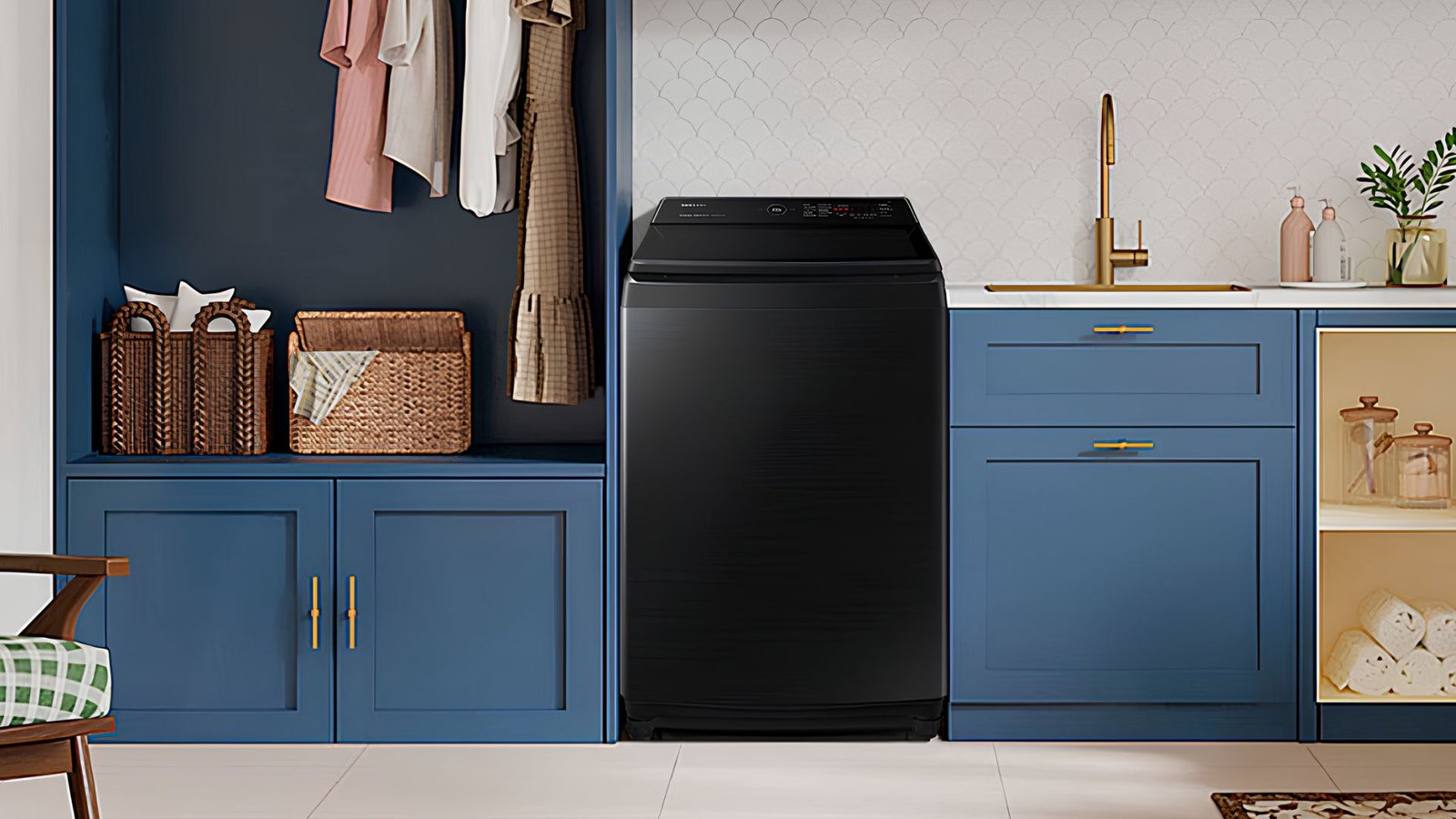 A imagem mostra uma lavanderia moderna e bem organizada, com uma lavadora de roupas de carregamento superior na cor preta no centro. O ambiente tem armários azul-escuros com puxadores dourados, além de uma bancada branca com uma pia e torneira dourada à direita da lavadora. À esquerda, há um espaço para pendurar roupas e cestos de vime para armazenamento. A decoração inclui pequenos frascos e plantas, criando um ambiente elegante e funcional.