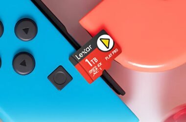 Um cartão de memória microSD vermelho Lexar de 1TB está posicionado acima de dois Joy-Cons azul e vermelho. O texto "Lexar", "1TB", "microSD EX PLAY PRO XC I" e um triângulo amarelo são visíveis no cartão.