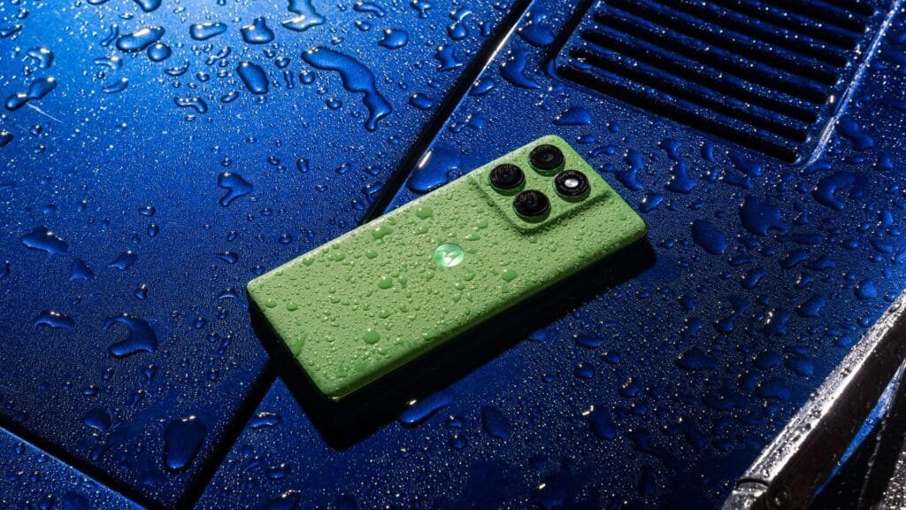 Um smartphone verde limão, o Motorola Edge 60 5G, repousa sobre o que parece ser o capô azul metálico de um carro esportivo, adornado com gotas d'água. O módulo da câmera, com seus quatro círculos que abrigam um conjunto triplo de câmeras e o flash LED, se destaca na parte superior, enquanto o logo da Motorola está centralizado na traseira.