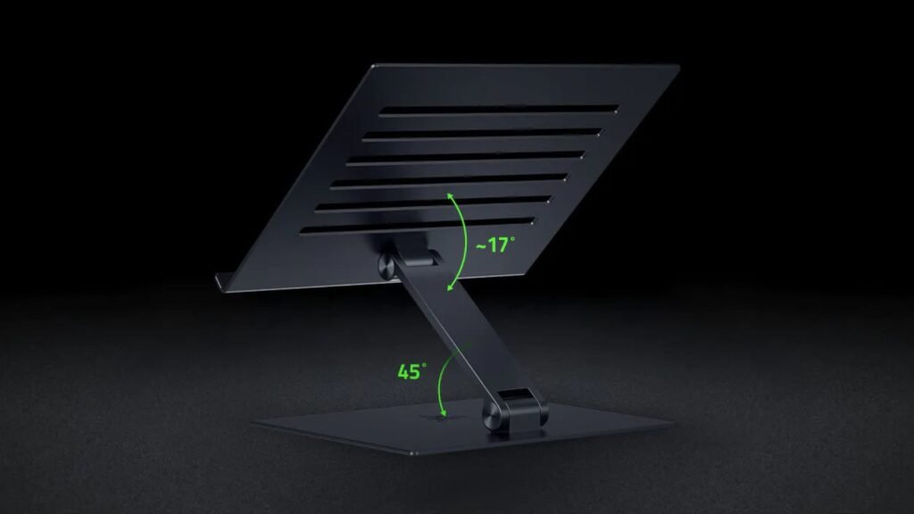 O Suporte Ajustável para Laptop da Razer é exibido em um fundo preto, mostrando um design inclinado com ranhuras para ventilação e feito de material preto fosco. A imagem destaca dois ângulos ajustáveis com setas verdes e rótulos: a articulação do suporte com 45° e a superfície superior com -17°, indicando a faixa de posicionamento ergonômico do laptop.