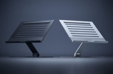 Imagem exibe o Razer Laptop Stand em duas variantes de cor: uma em tom de grafite e outra em tom prateado. Ambas as versões apresentam um design elegante e funcional, com uma base plana e um suporte inclinado para elevar o laptop a uma altura de visualização mais confortável. A superfície do suporte é adornada com ranhuras horizontais para auxiliar na ventilação do laptop. O logo da Razer pode ser visto no canto inferior direito do suporte prateado, indicando a marca do produto.