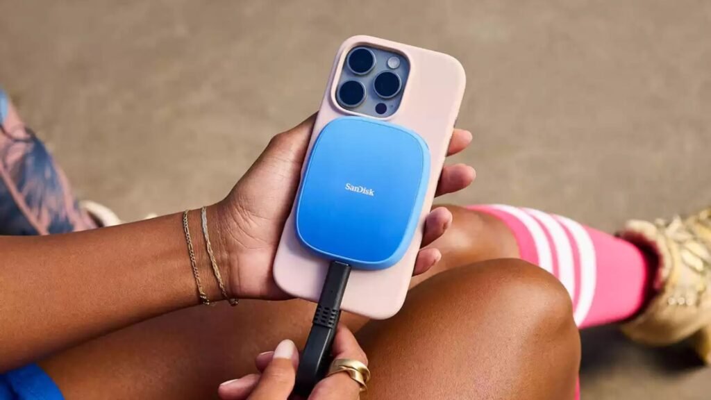 Uma pessoa segura um iPhone azul com capa rosa e um SSD portátil SanDisk Creator Phone azul claro conectado à parte de trás por um cabo preto.