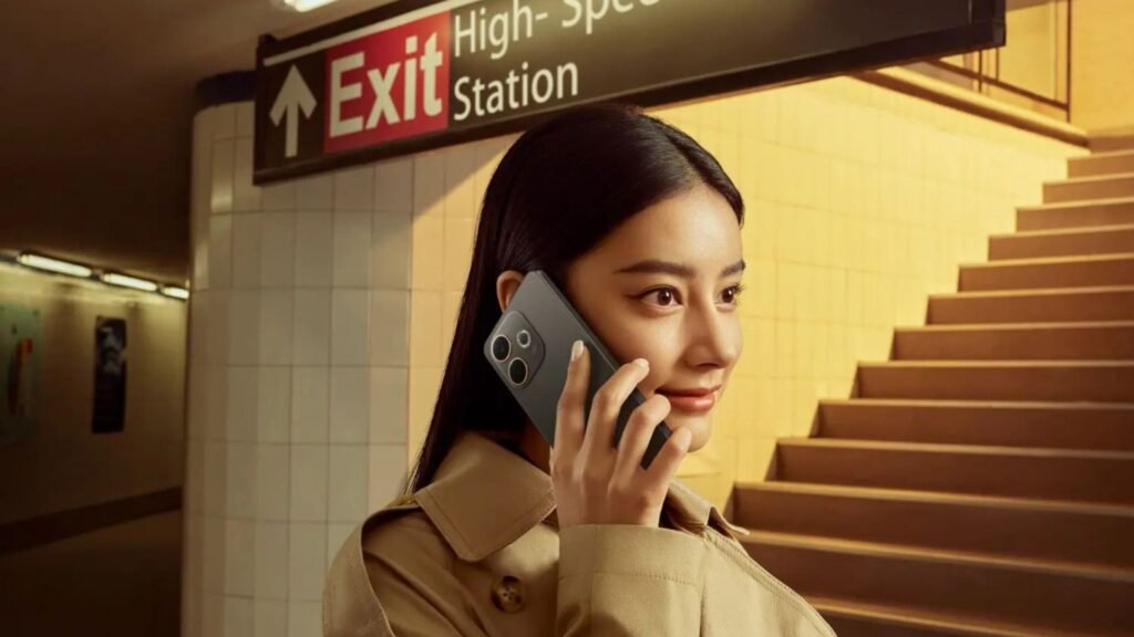 Uma mulher com aparência Leste-Asiática, de cabelos escuros e vestindo um sobretudo bege, está em uma estação de metrô. Ela segura um smartphone OPPO A5 Pro 5G de cor cinza junto ao ouvido, como se estivesse em uma ligação, e olha para o lado com um leve sorriso. Ao fundo, há uma escadaria e uma placa indicando "Exit" (Saída).
