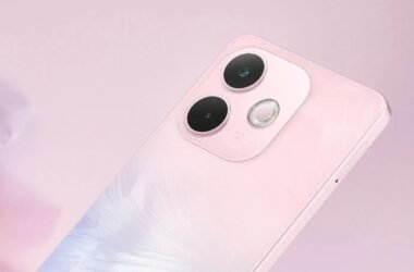 Close-up em ângulo da parte traseira do smartphone OPPO A5 Pro 5G. O aparelho tem um acabamento perolado em tons de rosa claro, com um reflexo azulado na parte inferior esquerda. O módulo de câmera, com duas lentes pretas grandes e um flash circular, está em destaque. O fundo é um rosa sólido e suave que complementa a cor do telefone.