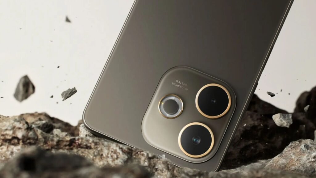 Close-up da parte traseira do smartphone OPPO A5 Pro 5G na cor cinza-escuro. O aparelho está apoiado sobre pedras e cascalho, com pequenos fragmentos de rocha suspensos no ar ao seu redor, criando uma cena que sugere alta durabilidade e resistência. O foco principal é o módulo de câmera com duas lentes grandes contornadas por anéis dourados.