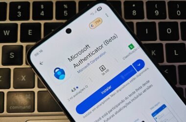 Um smartphone está deitado sobre o teclado preto de um notebook. Na tela do celular, está aberta a página de instalação do aplicativo de senhas "Microsoft Authenticator (Beta)" na Google Play Store. A interface está em português, e o botão azul "Instalar" está em destaque. O teclado ao fundo tem as teclas "option" e "command" parcialmente visíveis.