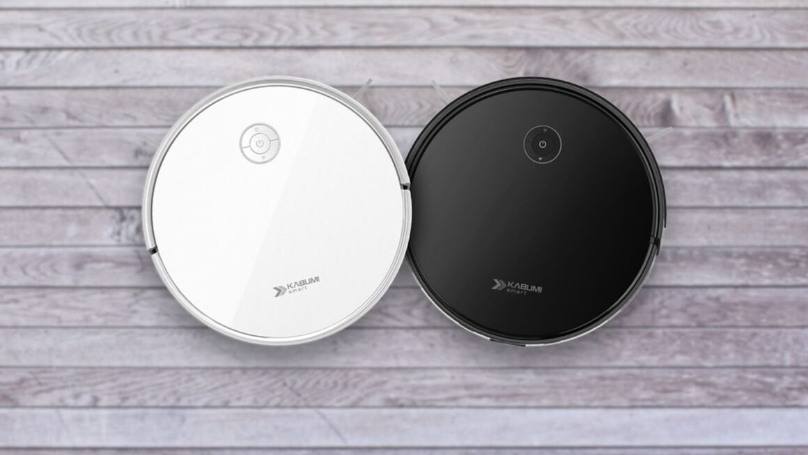 Duas imagens aéreas de aspiradores de pó robôs redondos KaBuM! Smart 550, idênticos em design, mas com cores diferentes. O aspirador à esquerda é branco e o da direita é preto. Ambos possuem um painel de controle simples no topo e a marca "KaBuM! SMART" impressa. Eles estão lado a lado, sobre um piso de madeira clara.