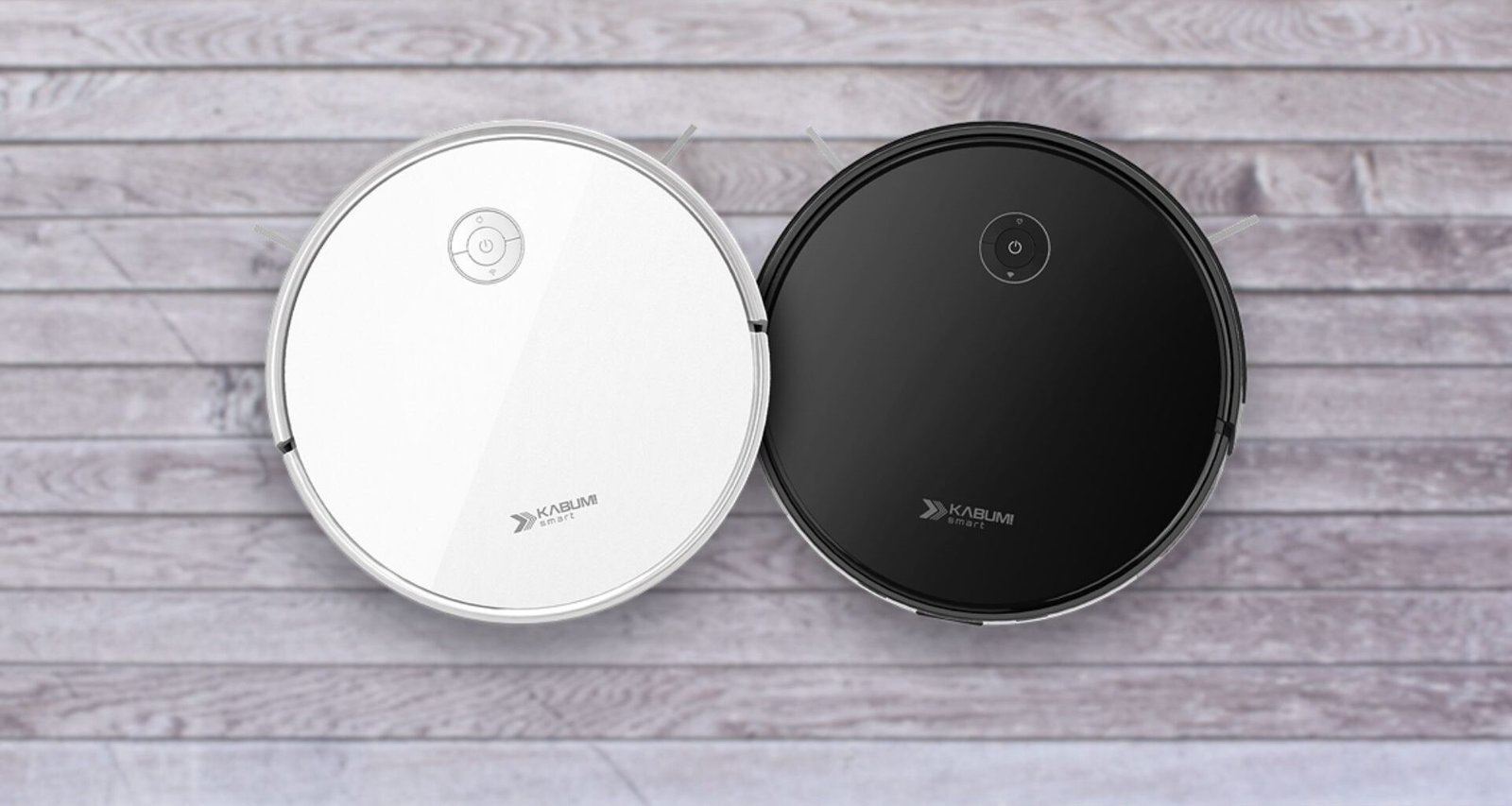 Duas imagens aéreas de aspiradores de pó robôs redondos KaBuM! Smart 550, idênticos em design, mas com cores diferentes. O aspirador à esquerda é branco e o da direita é preto. Ambos possuem um painel de controle simples no topo e a marca "KaBuM! SMART" impressa. Eles estão lado a lado, sobre um piso de madeira clara.