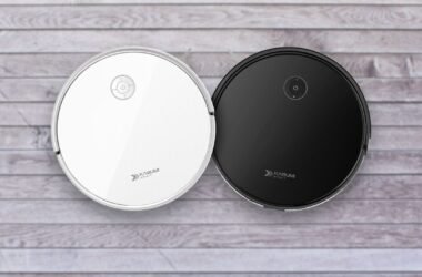 Duas imagens aéreas de aspiradores de pó robôs redondos KaBuM! Smart 550, idênticos em design, mas com cores diferentes. O aspirador à esquerda é branco e o da direita é preto. Ambos possuem um painel de controle simples no topo e a marca "KaBuM! SMART" impressa. Eles estão lado a lado, sobre um piso de madeira clara.