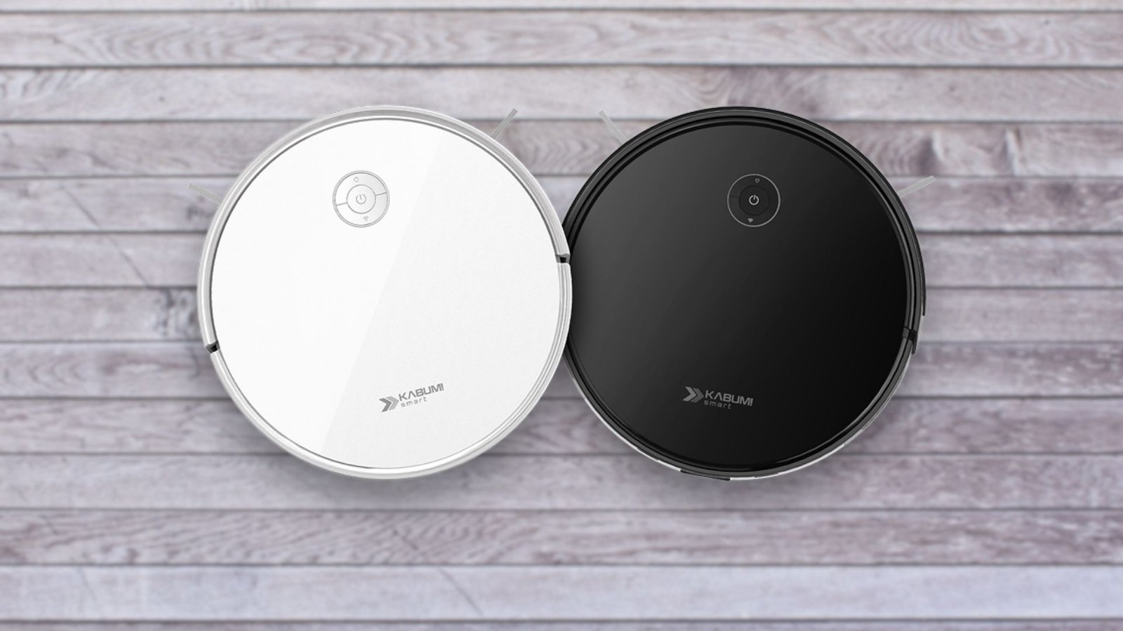 Duas imagens aéreas de aspiradores de pó robôs redondos KaBuM! Smart 550, idênticos em design, mas com cores diferentes. O aspirador à esquerda é branco e o da direita é preto. Ambos possuem um painel de controle simples no topo e a marca "KaBuM! SMART" impressa. Eles estão lado a lado, sobre um piso de madeira clara.