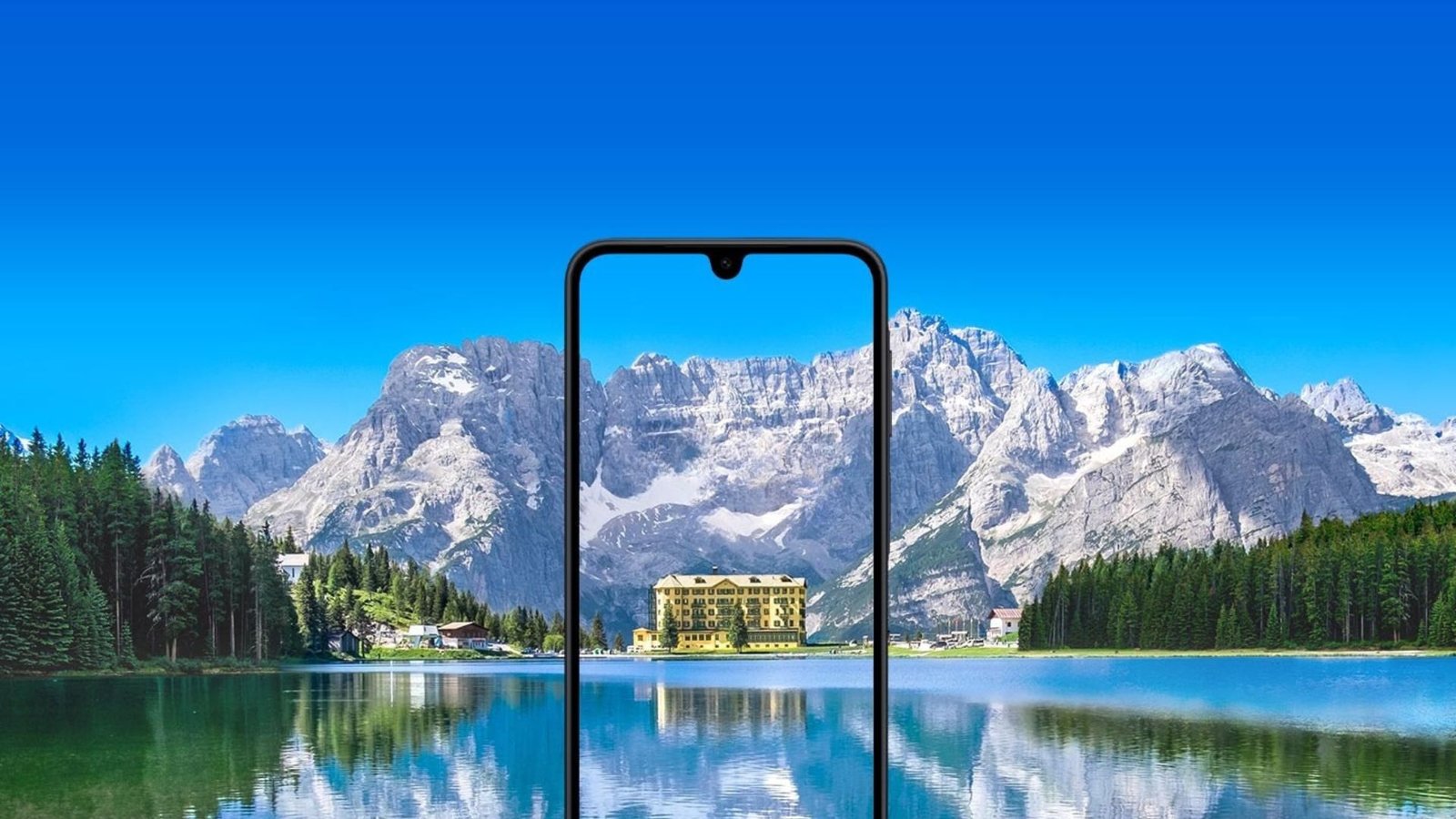 Um smartphone Samsung Galaxy A17 com um entalhe em forma de gota d'água está centralizado em primeiro plano. A tela do telefone exibe um prédio com fachada amarela e múltiplas janelas, cercado por árvores. O prédio parece estar localizado próximo a um corpo de água, e seu reflexo é visível na tela. O fundo da imagem é uma paisagem deslumbrante, com um grande e calmo lago em primeiro plano e uma cordilheira com picos nevados sob um céu azul brilhante ao fundo. A tela do celular aparece mostrando uma vista ampliada e recortada do prédio e de seus arredores imediatos a partir da paisagem do fundo, criando um efeito de moldura dentro de uma moldura. A imagem geral possui uma paleta de cores vibrante e aprimorada.