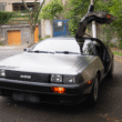 Carro esportivo DeLorean DMC-12 de aço inoxidável com a porta asa de gaivota do motorista aberta, estacionado em uma rua de paralelepípedos durante o dia
