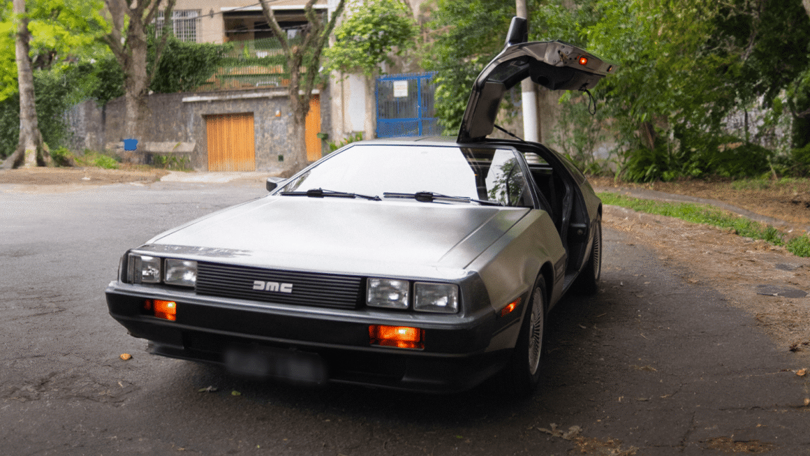 Carro esportivo DeLorean DMC-12 de aço inoxidável com a porta asa de gaivota do motorista aberta, estacionado em uma rua de paralelepípedos durante o dia