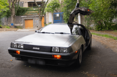 Carro esportivo DeLorean DMC-12 de aço inoxidável com a porta asa de gaivota do motorista aberta, estacionado em uma rua de paralelepípedos durante o dia
