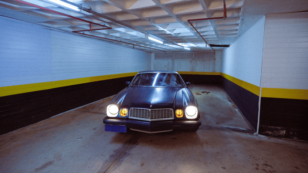 Chevrolet Camaro Z/28 azul de 1979 estacionado em uma garagem subterrânea com faróis acesos.